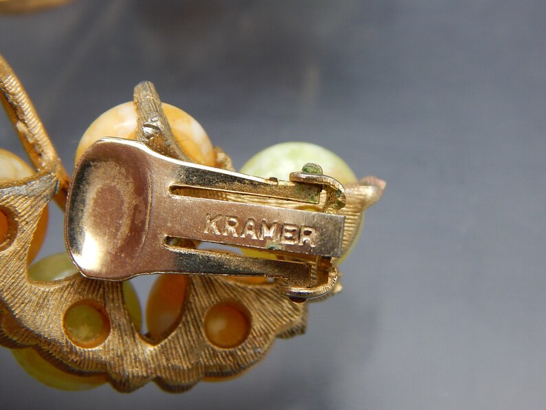May include: Gold tone clip-on earrings with a cluster of yellow and green stones. The back of the earrings are marked "KRAMER".