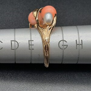 Pu&ograve; includere: Anello in oro con tre pietre di corallo e perla. L'anello &egrave; posto su un righello di metallo con segni di misurazione.