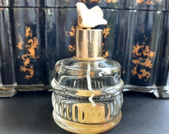 May include: A clear glass bottle with a gold top and a white ceramic stopper. The bottle has a textured design and is filled with a clear liquid.