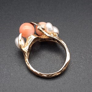 Pu&ograve; includere: Un anello d'oro con un design a forma di ramo incastonato con tre perle di corallo rosa e tre perle bianche.