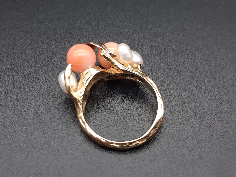 Pu&ograve; includere: Un anello d'oro con un design a forma di ramo incastonato con tre perle di corallo rosa e tre perle bianche.