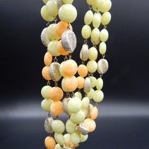 May include: A multi-strand necklace made of light yellow and orange glass beads. The beads are round and have a slightly textured surface. The necklace is strung on a gold chain.