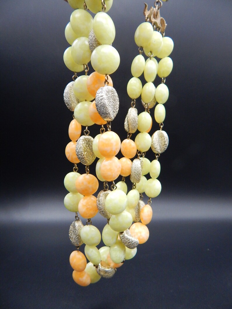 May include: A multi-strand necklace made of light yellow and orange glass beads. The beads are round and have a slightly textured surface. The necklace is strung on a gold chain.