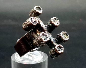May include: A silver-toned metal ring featuring a textured, organic surface with five distinct, raised cylindrical prongs extending from the center. The metal has a dark, oxidized finish in the crevices, contrasting with the polished edges.