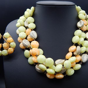 May include: A multi-strand necklace and matching earrings made of light green and peach colored beads. The beads are oval shaped and have a textured surface. The necklace is approximately 18 inches long.