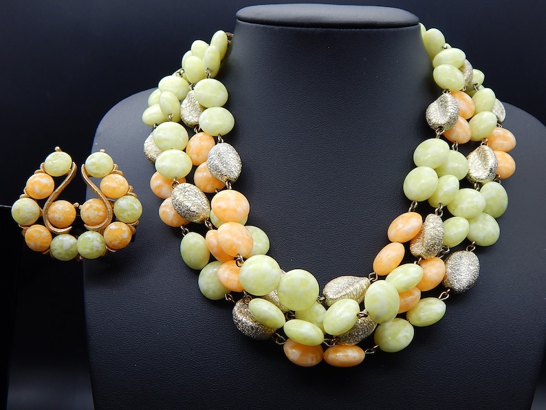 May include: A multi-strand necklace and matching earrings made of light green and peach colored beads. The beads are oval shaped and have a textured surface. The necklace is approximately 18 inches long.