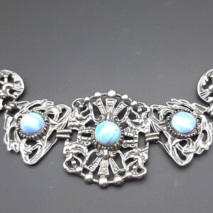 Può includere: Bracciale argentato con intricati disegni a filigrana e tre pietre cabochon azzurre. Il bracciale ha una chiusura e misura circa 17,78 cm di lunghezza.