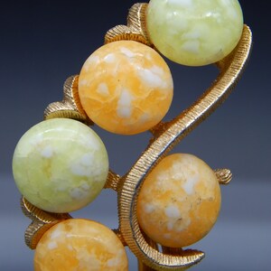 May include: A gold-tone brooch with a swirl design features six round, white and orange, marbled stones.