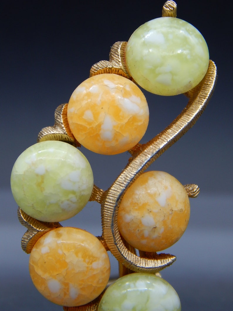 May include: A gold-tone brooch with a swirl design features six round, white and orange, marbled stones.