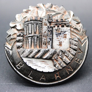 May include: A black wooden carved ornament depicting Blarney Castle, a popular tourist attraction in Ireland. The castle is carved in detail with a textured background.