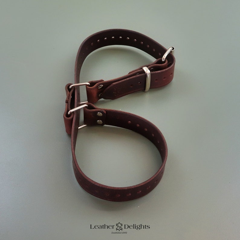 May include: A dark brown leather dog collar with silver-colored metal hardware. The collar is made of thick leather and has several holes for adjustment. The image is taken from a top-down perspective.