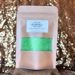 Puede incluir: Una bolsa de papel marrón con una etiqueta que dice "Little Grey Witch Cut & Clear Purify Purge Cleanse Fragranced Epsom Salts". La bolsa contiene sales de Epsom verdes.