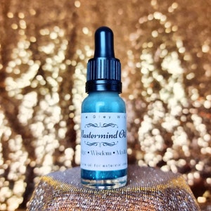 Puede incluir: Un pequeño frasco de vidrio azul con un gotero negro. El frasco tiene una etiqueta blanca que dice "Mastermind Oil" y "Conocimiento, Sabiduría, Meditación". El frasco está sobre una superficie dorada brillante.