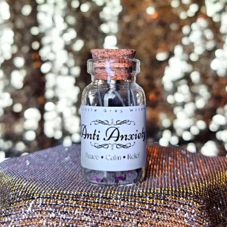 Puede incluir: Una peque&ntilde;a botella de vidrio con un tap&oacute;n de corcho llena de cristales y hierbas. La etiqueta dice "Little Gray Witch Anti Anxiety Peace Calm Relief".