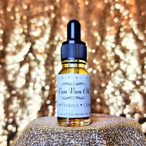 Può includere: Una piccola bottiglia di vetro con un contagocce riempita di un liquido dorato. L'etichetta riporta "Van Van Oil" e "Protect - Clean". La bottiglia è appoggiata su una superficie dorata scintillante.