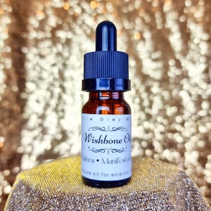 May include: A small brown glass bottle with a black dropper top. The bottle is labeled "Wishbone Oil" and says "Wishes - Manifestation" and "Nature oil for external use only".