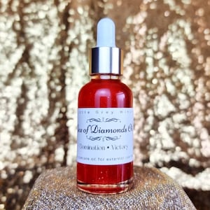 Può includere: Una piccola bottiglia di vetro con un contagocce d'argento riempita di un liquido rosso. L'etichetta recita "Ace of Diamonds Oil Domination - Victory" e "Tincture oil for external use only".