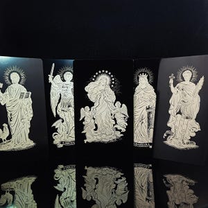 May include: Five black and white religious cards are displayed. Each card has a detailed illustration of a saint or angel, with intricate linework and a halo effect. The cards are arranged in a row, with their reflections visible.