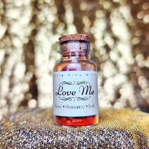 Pode incluir: Uma pequena garrafa de vidro com rolha, cheia de conteúdo vermelho. O rótulo diz "Love Me" com as palavras "Love, Romance, Lust" abaixo. A garrafa está rotulada como "Little Grey Witch".