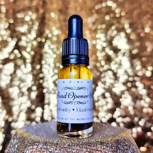 Puede incluir: Una pequeña botella de vidrio con un gotero negro en la parte superior, llena de un líquido transparente. La botella tiene una etiqueta blanca que dice "Road Opener Oil" y "Opportunity - Manifestation" con el texto "Pure oil for external use" en la parte inferior.