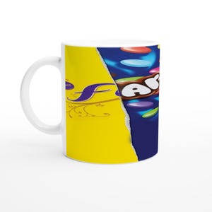 May include: A white ceramic mug with a yellow and blue design. The mug features a torn design with the words "Ferrero Rocher" on the yellow side and "Aero" on the blue side. The blue side also features a chocolate bar and colorful candy.