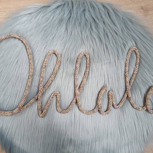 May include: A gold glitter wire word art spelling "Oh Lala" on a light blue fuzzy background.