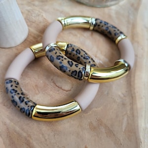Può includere: Due braccialetti beige e dorati con un motivo a stampa leopardata. I braccialetti sono impilati uno sopra l'altro.