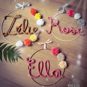 May include: Three knitted name wreaths with pom-poms. The names are "Elle", "Rose", and "Lola".