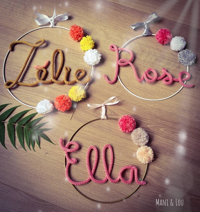 May include: Three knitted name wreaths with pom-poms. The names are "Elle", "Rose", and "Lola".