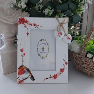 May include: White wooden picture frame featuring a painted robin and red berry branch design. Two heart-shaped ornaments hang from the top. The frame has the text "Ashley Ever After" and "Shropshire England".