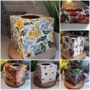 May include: A collection of square and rectangular tissue box covers featuring various patterns including yellow and blue wildflowers, red tulips, purple flowers, citrus fruits, blue stars, and green foliage with red berries, each with a circular top opening.