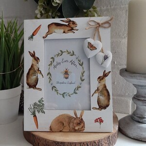 May include: White wooden picture frame decorated with rabbit and carrot illustrations. The frame features the text "Apley Ever After... Shropshire England" and two heart-shaped ornaments. The frame is displayed on a wooden slice.