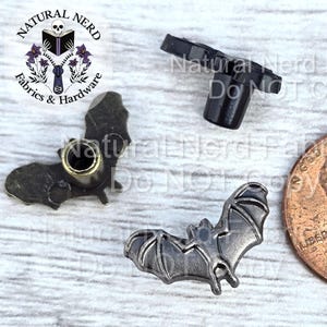 May include: A collection of metal bat-shaped charms and a black plastic clasp. A US penny is included for size comparison. The charms are in various shades of gray and bronze. The image includes the text "Natural Nerd Fabrics & Hardware".