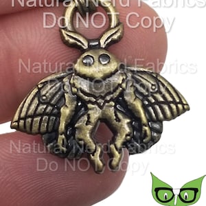 Könnte beinhalten: Antiker goldfarbener Metall-Anhänger mit einem detaillierten Mottiv-Design mit ausgebreiteten Flügeln. Der Anhänger hat oben eine Schlaufe zum Anbringen an einer Halskette oder einem Armband.