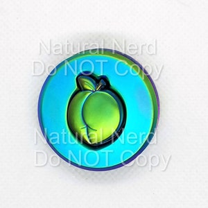 May include: A round, iridescent, metallic charm with a green peach design. The charm has a blue background and the text "Natural Nerd Do NOT Copy" is printed around the edge.