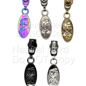 Five zipper pulls with oval-shaped charms featuring a man's face. The charms are in different colors: iridescent, silver, gold, black, and chrome.