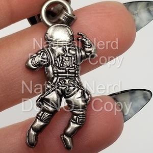 May include: Silver astronaut charm with a detailed design, wearing a spacesuit and helmet. The charm is attached to a silver chain.