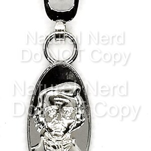 Silver zipper pull with an oval-shaped charm featuring a detailed image of a person's face.