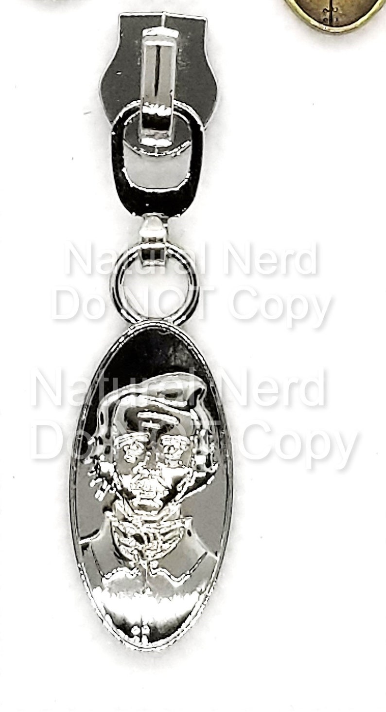 Silver zipper pull with an oval-shaped charm featuring a detailed image of a person's face.