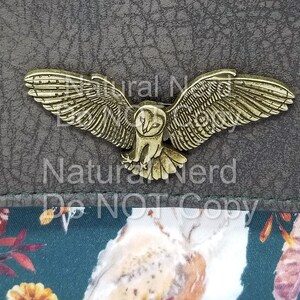A bronze-toned metal owl magnetic snap with detailed wings and a realistic owl design. The snap is on a brown textured surface.