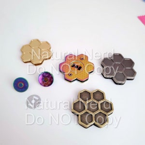 May include: Assortment of hexagonal shaped metal pieces in gold, silver, and iridescent colors. The pieces have a honeycomb pattern and are arranged on a white surface.