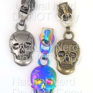 May include: Three zipper pulls with skull charms. The skulls are silver, bronze, and iridescent rainbow. The zipper pulls are silver, bronze, and rainbow.