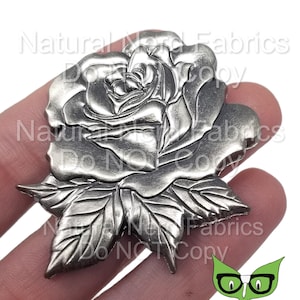 May include: A silver metal rose with detailed leaves. The rose is a decorative embellishment for crafts and jewelry making.