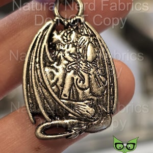 May include: Silver-toned metal pendant featuring a detailed depiction of a gargoyle with wings, sitting with its head resting on its hands.