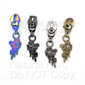 Puede incluir: Cuatro tiradores de cremallera con un diseño de abeja y panal. Los tiradores están disponibles en cuatro acabados: iridiscente, negro, plateado y dorado.