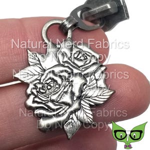 Peut inclure: Breloque de tirette de fermeture éclair en argent avec un motif détaillé de deux roses avec des feuilles.