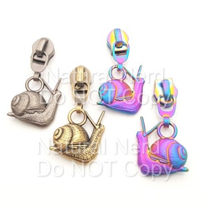 Puede incluir: Cuatro tiradores de cremallera con dijes de caracol. Los caracoles son de diferentes colores: plateado, dorado, morado iridiscente y azul iridiscente. Los tiradores de cremallera son de metal.