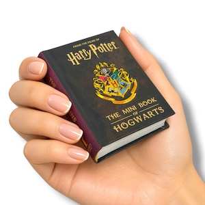 May include: A miniature book titled The Mini Book of Hogwarts from the films of Harry Potter. The cover is black with gold lettering and features a colorful Hogwarts school crest in the center. The spine is dark purple with gold text.
