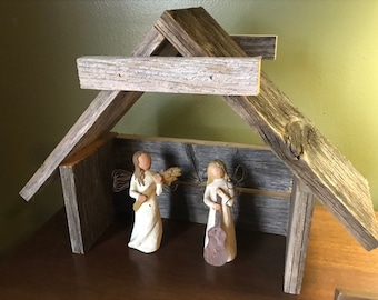 Può includere: Un presepe rustico in legno con due figurine di angeli. Un angelo tiene un gambo di grano e l'altro una chitarra.