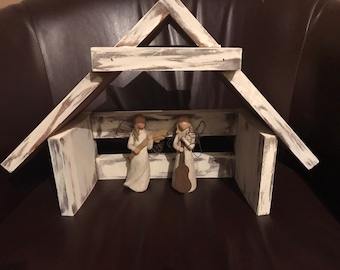Può includere: Un presepe in legno sbiancato con due figurine di angeli che tengono strumenti musicali. La scena è ambientata su uno sfondo di pelle marrone.